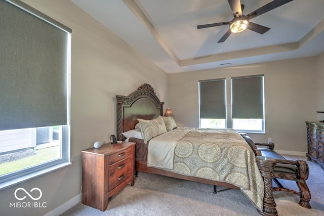 bedroom featuring multiple windows, light carpet, a tray ceiling, and baseboards
