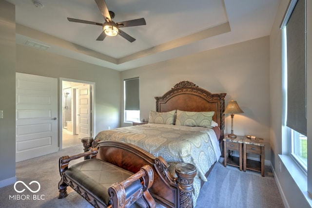 carpeted bedroom featuring a raised ceiling, ensuite bath, ceiling fan, and baseboards