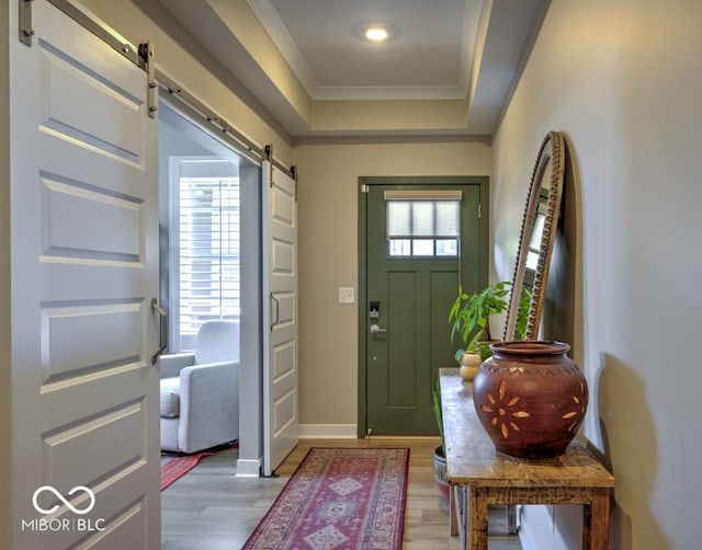 entrance foyer featuring a barn door, a tray ceiling, light wood-style floors, crown molding, and baseboards