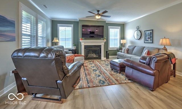 living room with wood finished floors, ceiling fan, crown molding, baseboards, and a glass covered fireplace
