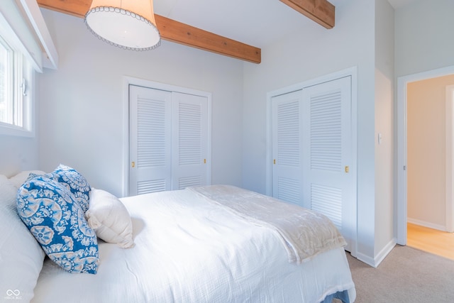 bedroom with beam ceiling, carpet floors, baseboards, and two closets