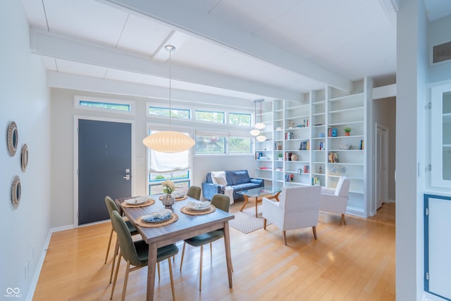dining space featuring beam ceiling, light wood finished floors, built in shelves, and baseboards