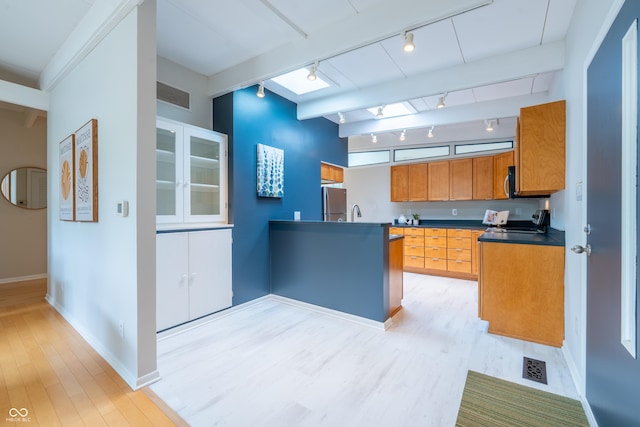 kitchen with rail lighting, light wood-type flooring, brown cabinets, baseboards, and dark countertops