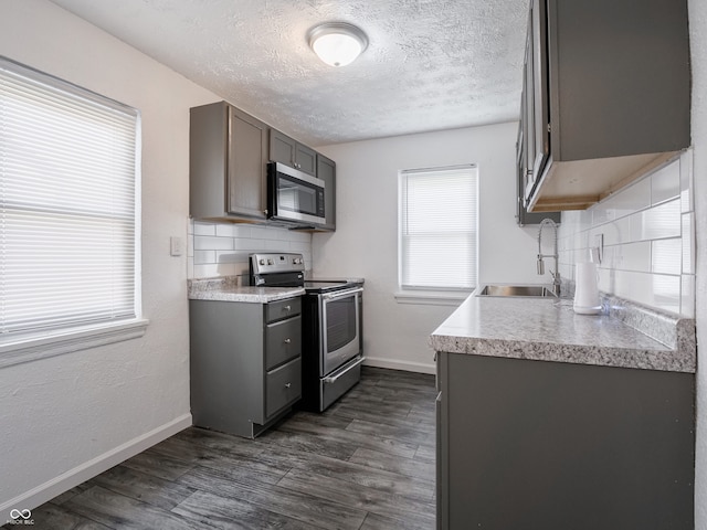 kitchen featuring appliances with stainless steel finishes, a sink, backsplash, baseboards, and gray cabinetry