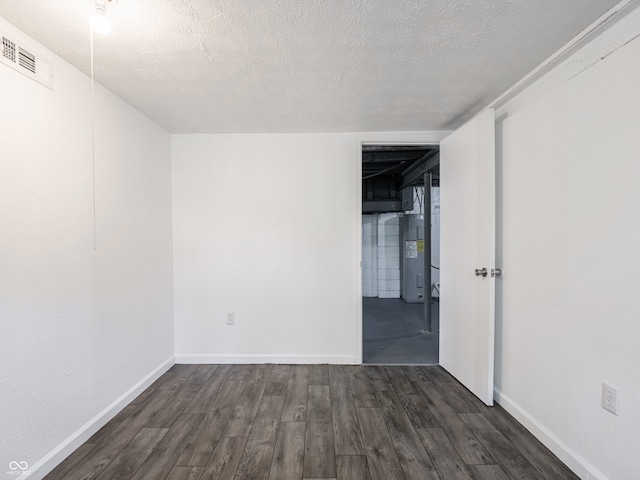 empty room featuring dark wood-style flooring, baseboards, a textured ceiling, and electric water heater