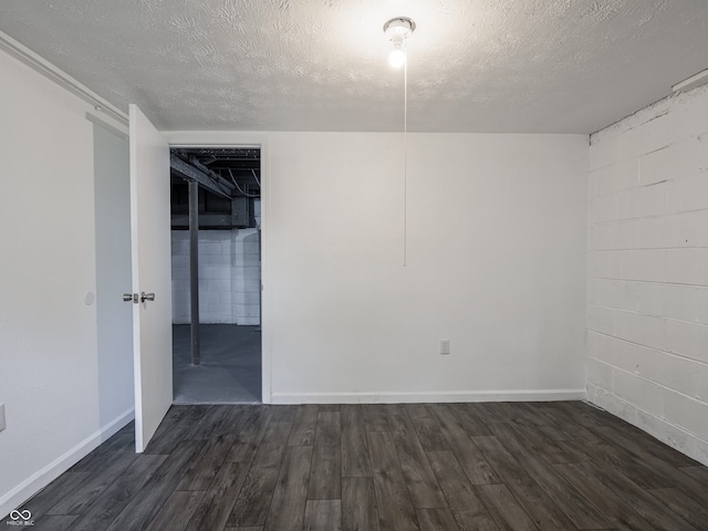 unfurnished bedroom featuring concrete block wall, dark wood finished floors, a textured ceiling, a closet, and baseboards