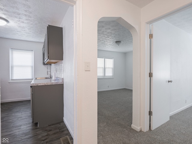 hall featuring a sink, a textured ceiling, arched walkways, and baseboards