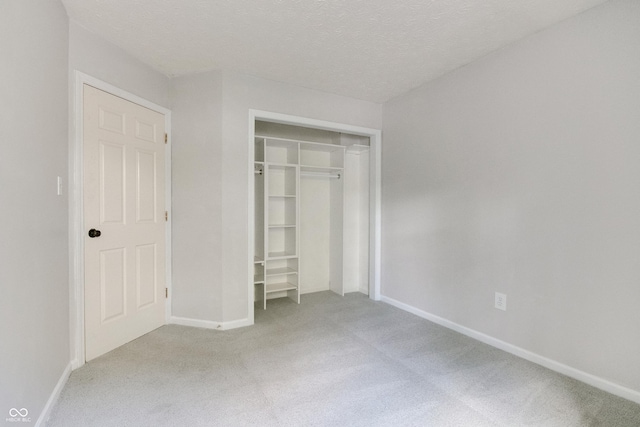 unfurnished bedroom with light colored carpet, baseboards, a closet, and a textured ceiling