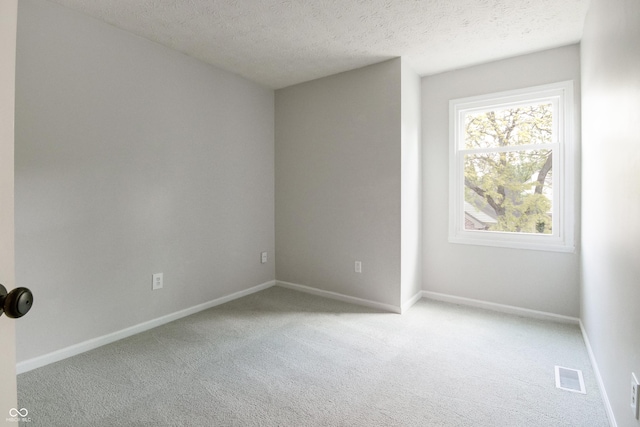 empty room with light colored carpet, a textured ceiling, and baseboards