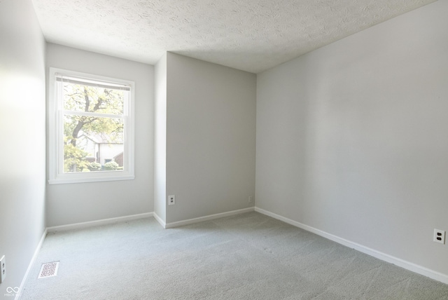 empty room with light carpet, a textured ceiling, and baseboards