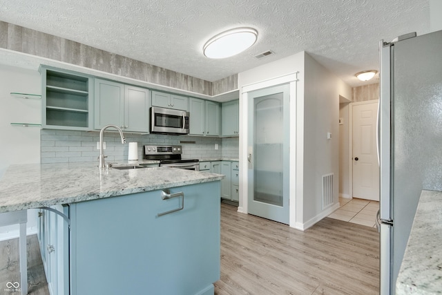 kitchen featuring appliances with stainless steel finishes, a sink, a peninsula, light wood-style floors, and tasteful backsplash