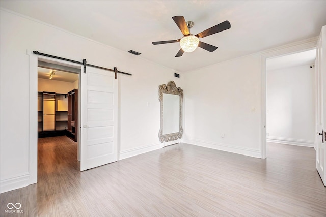 unfurnished room featuring a barn door, ceiling fan, wood finished floors, and baseboards