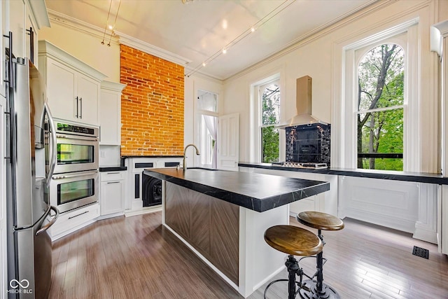 kitchen featuring dark countertops, exhaust hood, stainless steel appliances, ornamental molding, and wood finished floors