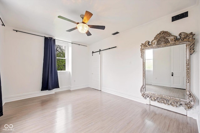 spare room with a barn door, a ceiling fan, wood finished floors, and baseboards