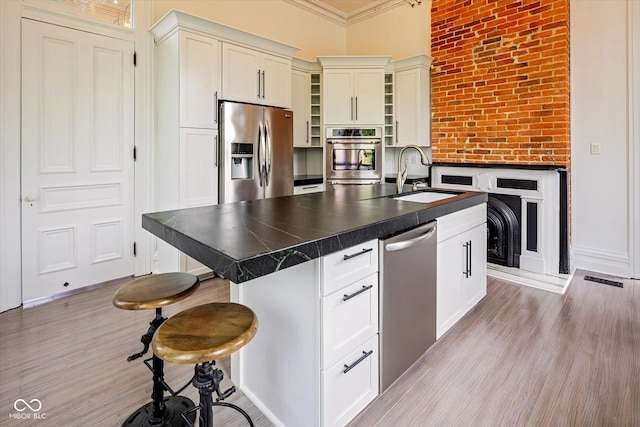kitchen featuring appliances with stainless steel finishes, a sink, dark countertops, light wood-style flooring, and ornamental molding