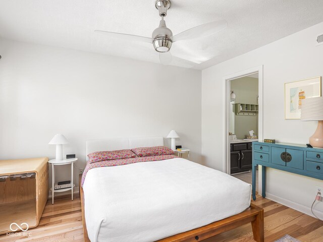 bedroom featuring light wood-type flooring, ensuite bath, and a ceiling fan