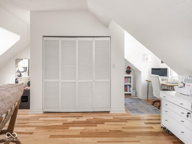 bedroom with vaulted ceiling, light wood-style floors, a desk, a closet, and baseboards