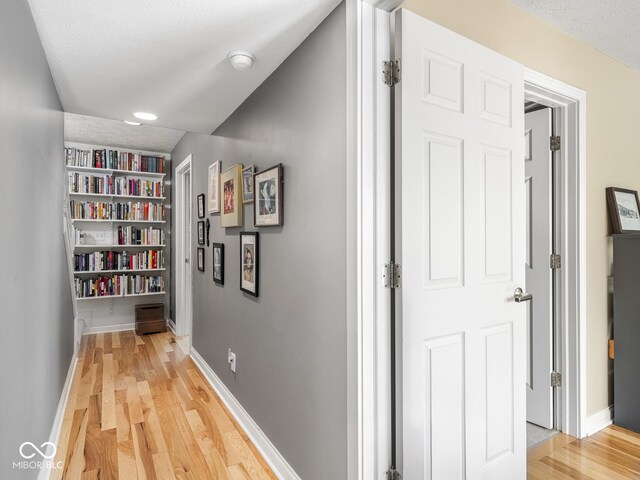 hall with baseboards, light wood-style floors, built in shelves, and a textured ceiling