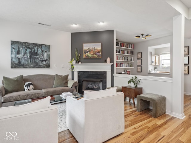 living room with wood finished floors, a tiled fireplace, built in shelves, and baseboards