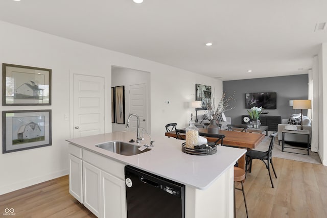 kitchen with a sink, black dishwasher, open floor plan, white cabinetry, and light wood finished floors