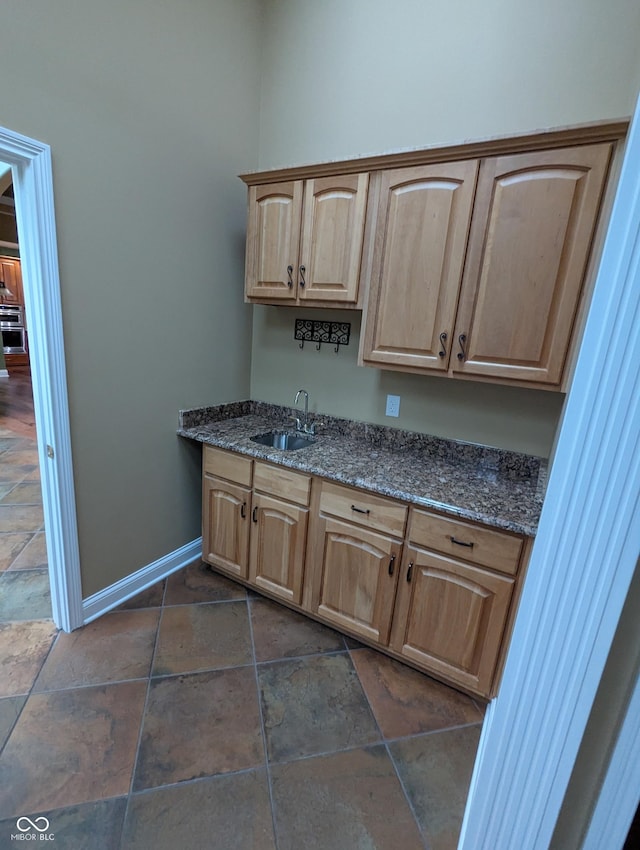 9640 Bramblewood Way, Carmel, IN 46032 - kitchen with a sink, light brown cabinetry, stone tile flooring, baseboards, and dark stone counters
