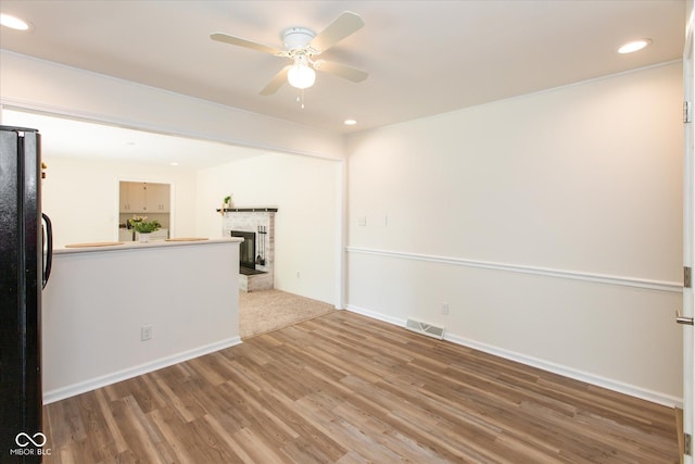 empty room with a ceiling fan, light wood finished floors, a fireplace with raised hearth, recessed lighting, and baseboards