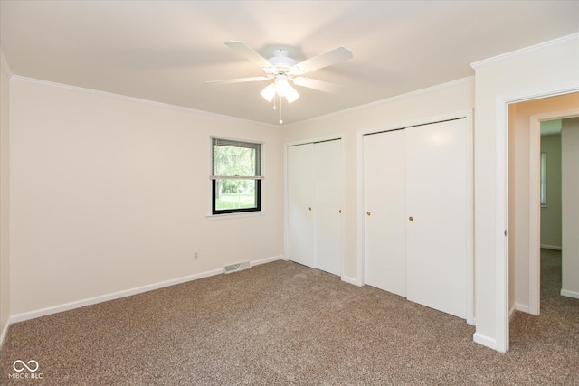 unfurnished bedroom with two closets, carpet, ornamental molding, and baseboards