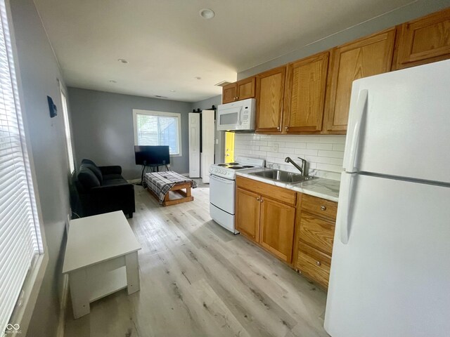 kitchen featuring white appliances, a sink, light wood-style floors, backsplash, and brown cabinetry