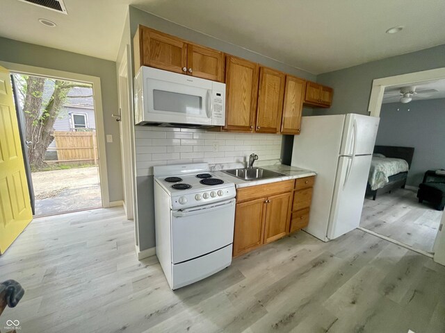 kitchen with white appliances, a sink, light wood-type flooring, tasteful backsplash, and light countertops