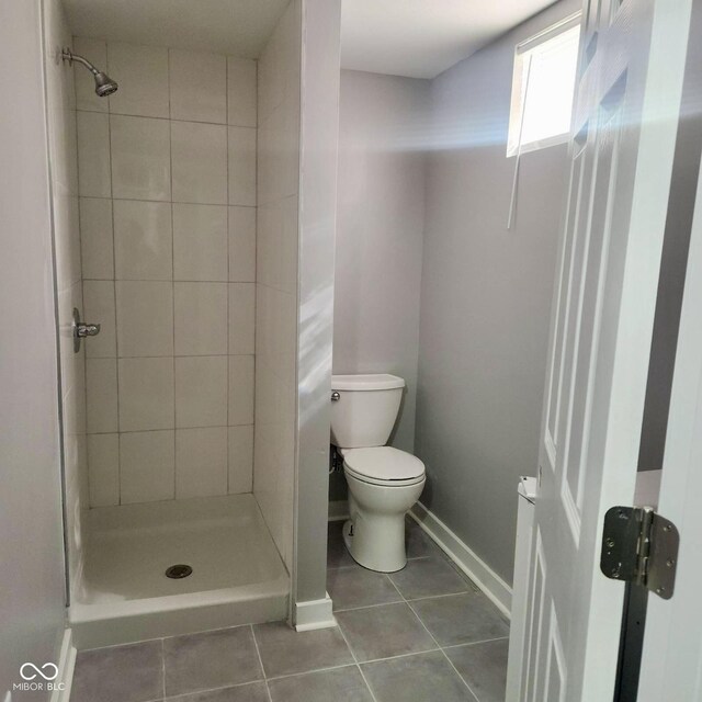 bathroom with tile patterned floors, toilet, a stall shower, and baseboards