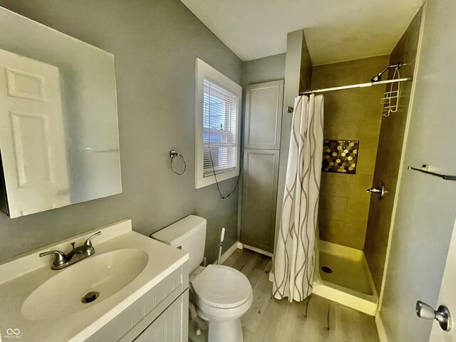 bathroom featuring wood finished floors, a stall shower, toilet, and vanity