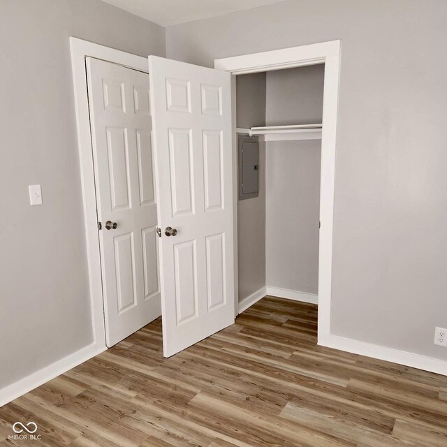 unfurnished bedroom featuring electric panel, wood finished floors, a closet, and baseboards