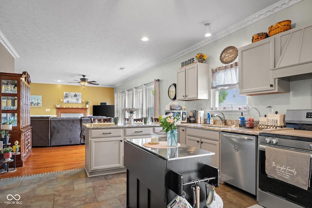 kitchen featuring appliances with stainless steel finishes, a sink, a ceiling fan, crown molding, and a peninsula