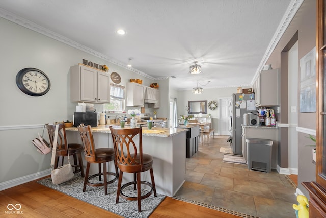 kitchen with a peninsula, appliances with stainless steel finishes, a breakfast bar, light stone counters, and ornamental molding