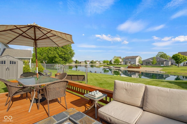 wooden terrace featuring a shed, a water view, outdoor dining area, and an outbuilding
