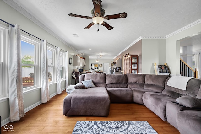living area with a ceiling fan, light wood-style flooring, ornamental molding, a textured ceiling, and baseboards