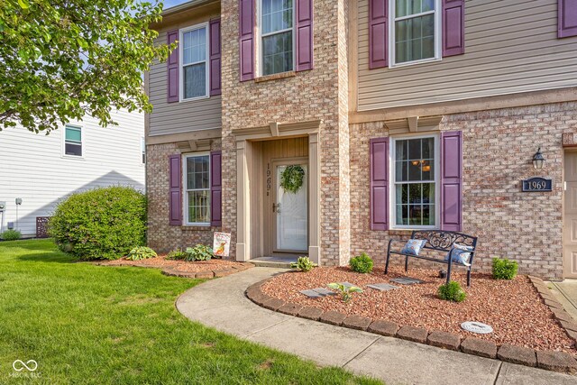 entrance to property featuring a lawn and brick siding