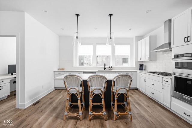 127 Monon Green Blvd, Carmel, IN 46032 - kitchen featuring appliances with stainless steel finishes, wall chimney exhaust hood, a breakfast bar area, decorative backsplash, and white cabinets