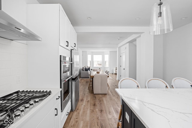 127 Monon Green Blvd, Carmel, IN 46032 - kitchen featuring wall chimney exhaust hood, stainless steel appliances, light wood-style floors, open floor plan, and white cabinets