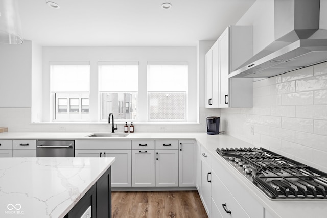 127 Monon Green Blvd, Carmel, IN 46032 - kitchen featuring wall chimney exhaust hood, appliances with stainless steel finishes, light stone counters, decorative backsplash, and light wood-style flooring