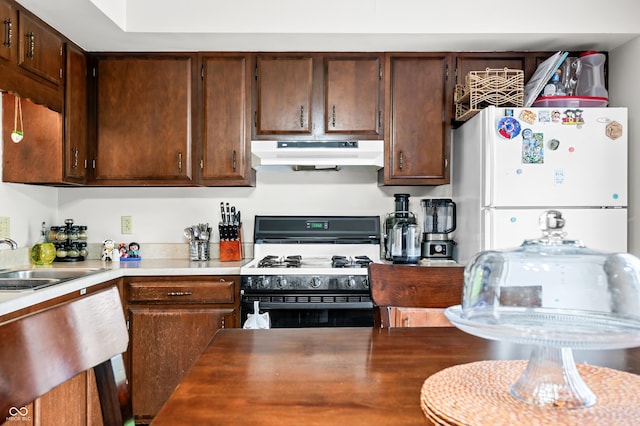 5120 Apache Ct, Columbus, IN 47203 - kitchen featuring under cabinet range hood, range with gas cooktop, a sink, freestanding refrigerator, and dark brown cabinetry