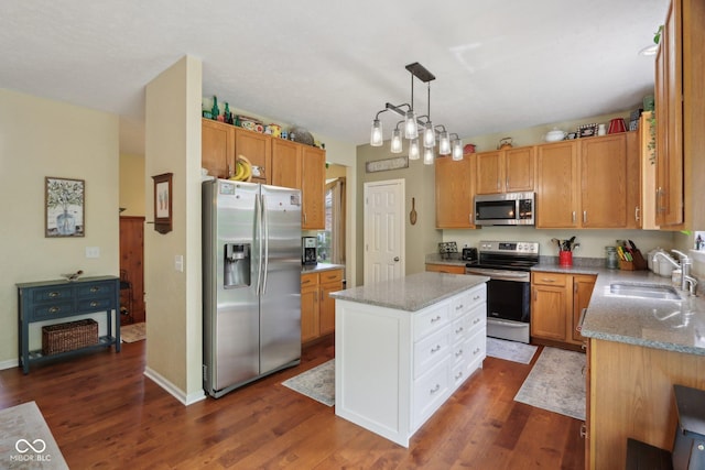 kitchen featuring appliances with stainless steel finishes, a sink, dark wood-type flooring, light stone counters, and a center island