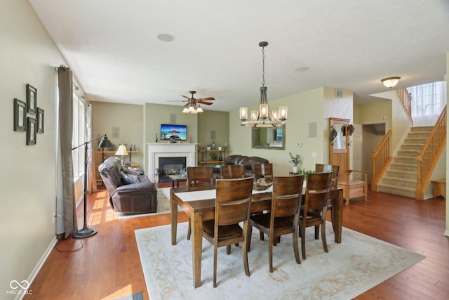 dining area with a glass covered fireplace, a ceiling fan, stairs, wood finished floors, and a chandelier