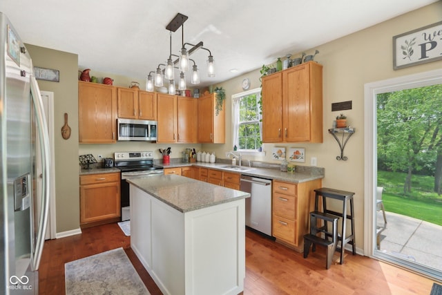 kitchen with stainless steel appliances, a sink, wood finished floors, a center island, and light stone countertops