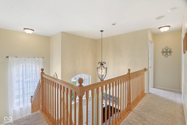 hallway with an upstairs landing, a chandelier, carpet, and baseboards