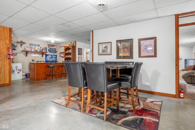 dining room with a bar, a drop ceiling, concrete floors, and baseboards