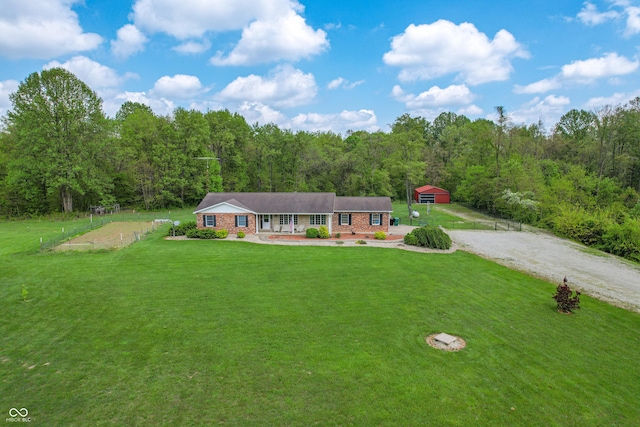 ranch-style home with a view of trees, brick siding, gravel driveway, and covered porch