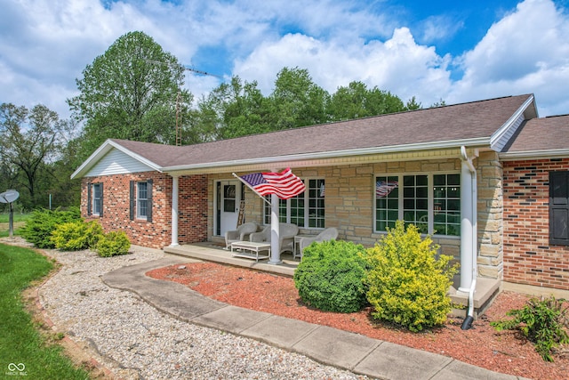 single story home with brick siding, roof with shingles, stone siding, and covered porch