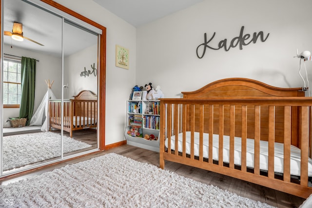 bedroom featuring wood finished floors, baseboards, a crib, and a closet