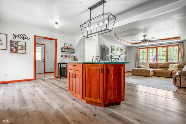 kitchen with baseboards, light wood-type flooring, a raised ceiling, and a ceiling fan